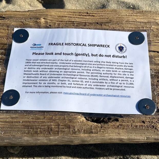Sign on a shipwreck timber saying, "Fragile Historical Shipwreck. Please look and touch (gently), but do not disturb!"