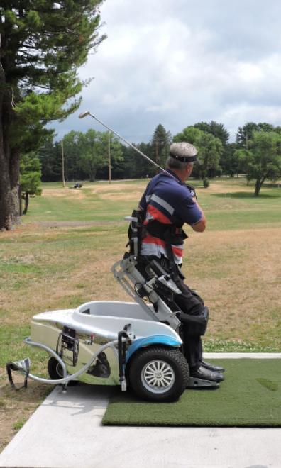 A man is using a ParaGolfer all-terrain wheelchair to raise himself to a standing position. He is swinging a golf club over his shoulder and looking down range.