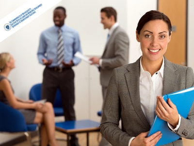 Female holding blue folder and smiling. Two men and one women talking in the background. 